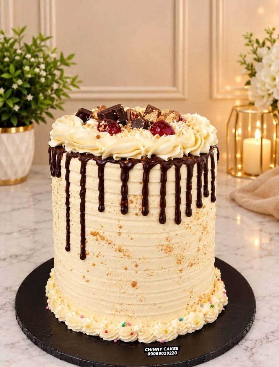 Cream cake topped with chocolate pieces, cherries and chocolate drip