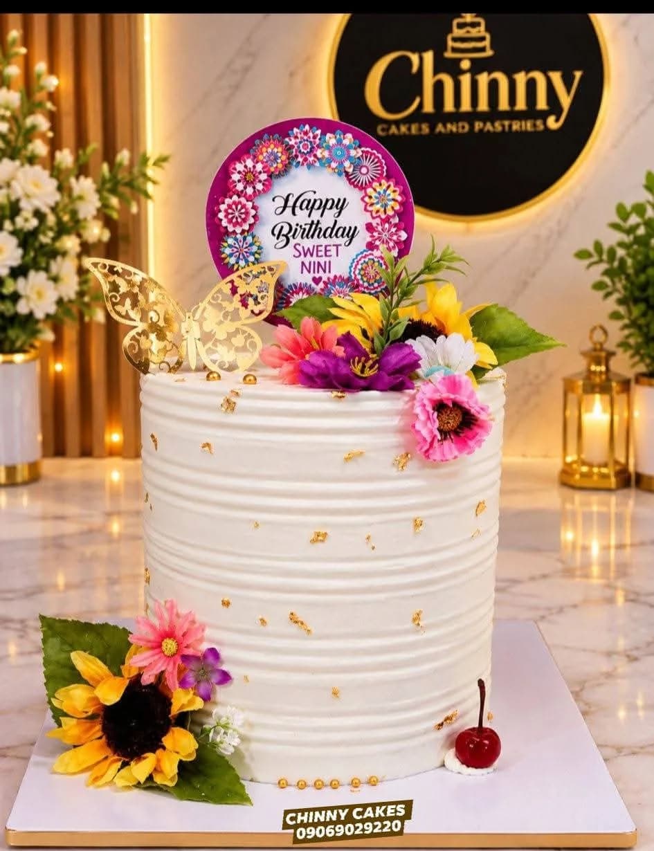 Tall white Chinny Cake decorated with colourful flowers, a gold butterfly and birthday topper