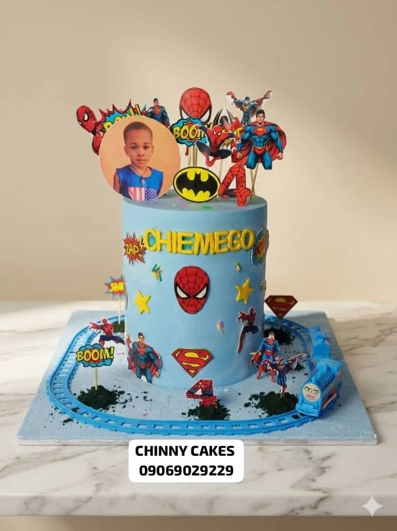 Blue children's birthday cake with superhero decorations and toy train detail